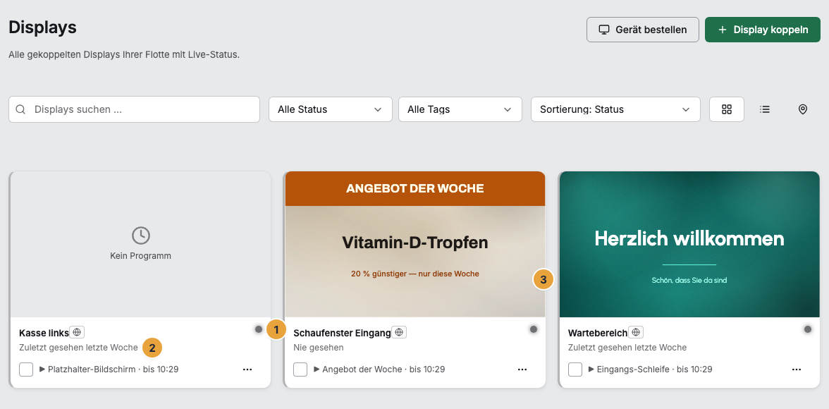 Die Flotte unter Displays in der Kachel-Ansicht mit drei Displays: der Statuspunkt neben dem Namen (1), darunter die Zeile „Zuletzt gesehen …“ (2) und rechts die Kachel eines Displays, das seine Playlist spielt, mit dem Bild des laufenden Inhalts (3)